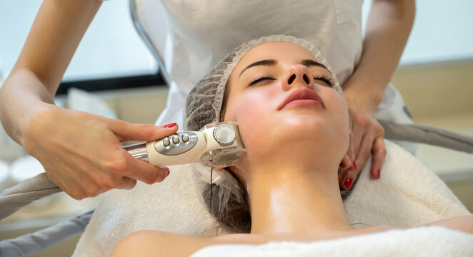 Close up of young woman receiving electric ultrusound facial massage at beauty salon. Woman with closed eyes getting rf-lifting in a beauty salon.