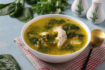 Soup with chicken, spinach and egg in white bowl on blue background