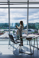 Attractive female blogger in a jacket with a modern smartphone in her hands, thoughtful and daydreaming, a young blogger holding a mobile phone, reflects on social media posts