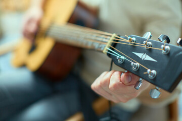 Close up professional male musician adjusts the sound on the guitar by hand, turning pegs by fingers on fingerboard