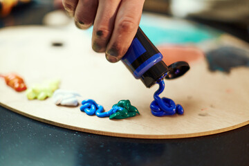 Close up painter hand squeeze acrylic blue paint from tube on wooden painting palette. Artist...