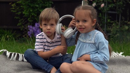 Two Happy Siblings boy ans girl listening to music on headphones outside in Garden. Children and technology. Brother and Sister. Love of music, dreams hobbies. Childhood, musicality, hobby. Friendship