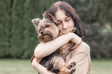 A cute girl with a Yorkshire terrier on the street. Hugs with your little dog in the park