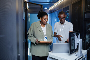 Waist up portrait of two black young people as IT engineers using laptop in server room while setting up network