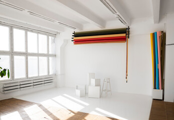 Sunny daylight photo studio interior with a huge panoramic vintage windows with set rolls of color background and white cubes on a floor. Professional equipment for studio photography.
