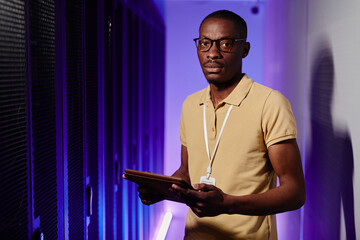 Waist up portrait of African American man inspecting data network in server room lit by neon light...