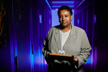 Waist up portrait of female network engineer holding tablet in server room and looking at camera