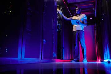 Full length portrait of African American system administrator setting up server network in data...
