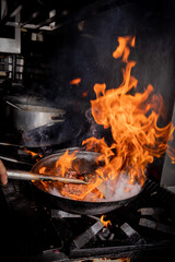 Manos que cocinan en un restaurant, con sarten sobre fuego. Salteado de carnes
