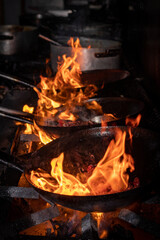 Manos que cocinan en un restaurant, con sarten sobre fuego. Salteado de carnes