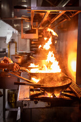Manos que cocinan en un restaurant, con sarten sobre fuego. Salteado de carnes