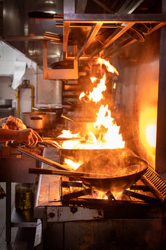 Manos que cocinan en un restaurant, con sarten sobre fuego. Salteado de carnes