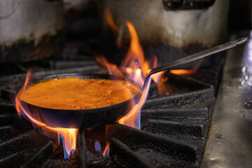 Manos que cocinan en un restaurant, con sarten sobre fuego. Salteado de carnes