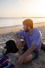 Jeune homme qui boit une bière sur la plage au soleil couchant