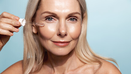 Close up of middle aged smiling woman, applies C-Serum with dropper, collagen anti-aging oil for...