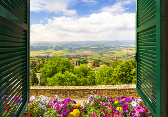 View through an open window with shutters out over the Tuscan countryside and medieval hilltop old town of San Gimignano, Italy.