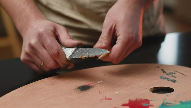 Artist sharpening a wooden pencil with a cutter knife, shavings fall on the painter palette. ProRes codec. Close-up