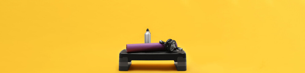 Step platform, mat, bottle of water and abdominal wheel on yellow background. Banner design