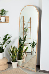 Stylish full length mirror and houseplants near white wall in room