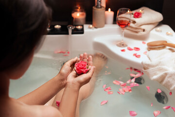 Woman holding rose flower while taking bath, closeup. Romantic atmosphere