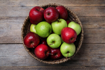 Fresh ripe green and red apples with water drops in wicker bowl on wooden table, top view