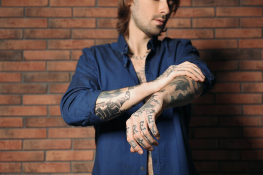 Young man with tattoos on body near brick wall, closeup