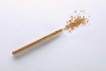 Glass tube with mustard seeds on white background, top view