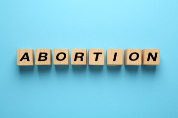 Fototapeta premium Word Abortion made of wooden cubes on light blue background, flat lay
