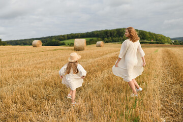 Mother plays with daughter in a field with wheat