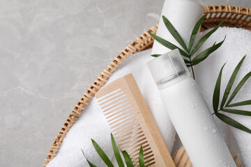 Dry shampoo sprays, towel and wooden comb with green leaves in wicker basket on light grey table, top view. Space for text - obrazy, fototapety, plakaty
