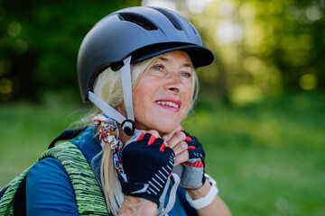 Fototapeta na wymiar Active senior couple riding bicycles at summer park, woman is putting on helmet, healthy lifestyle concept.