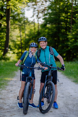 Portrait of active senior couple riding bicycles at summer park, standing on path and looking at...