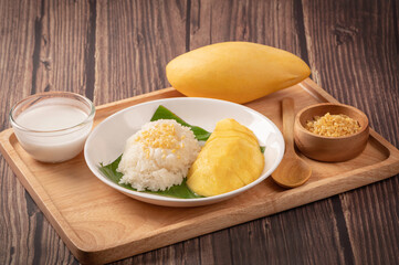 Mango sticky rice with coconut milk on wooden table.