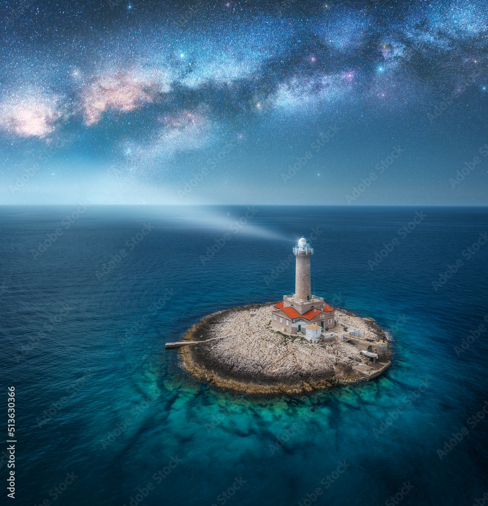 Wall mural lighthouse on smal island in the sea and milky way at night in summer. aerial view of beautiful ligh