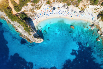 Obraz premium Aerial view of blue sea, rock, sandy beach with umbrellas at sunrise in summer. Porto Katsiki, Lefkada island, Greece. Beautiful landscape with sea coast, swimming people, trees, azure water. Top view