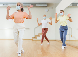 Fototapeta na wymiar Elderly woman in face mask learning aerobic dance with her younger relatives in studio.