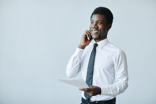 Minimal portrait of young black businessman speaking on phone against white background, copy space