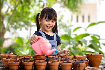 Adorable 3 years old asian little girl is watering the plant in the pots, concept of plant growing...
