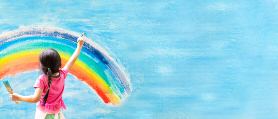 Banner of unidentified little girl is painting the colorful rainbow and sky on the wall and she...