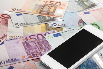 Blank screen smartphone which is placed on the pile of banknotes.