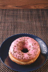 delicious round shaped bread with pink icing and colorful sprinkles on a dark plate ready for breakfast