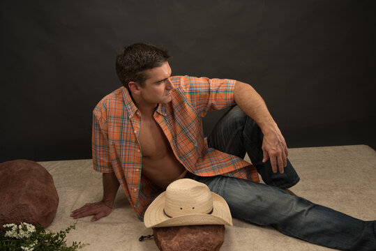 The attractive cowboy man is posing in a studio for the photo.