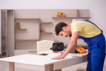 Young male carpenter repairing table at home