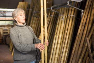 Focused interested senior woman looking for natural bamboo poles in horticultural market for landscaping in backyard or garden