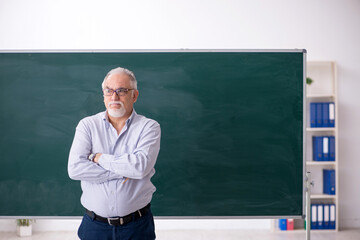 Old male teacher in front of green board