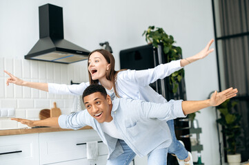 Fototapeta premium Multiracial happy couple in love, caucasian girl and latino guy, dressed in a modern casual clothes, have fun together at home in the kitchen, laugh, enjoy the weekend, experiencing positive emotions