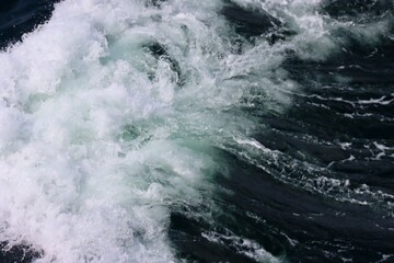 Fototapeta na wymiar Stern waves with white foam tips on greyish blue sea water, photo taken from aboard ship. Selective focus