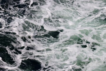 Stern waves with white foam tips on greyish blue sea water, photo taken from aboard ship. Selective focus