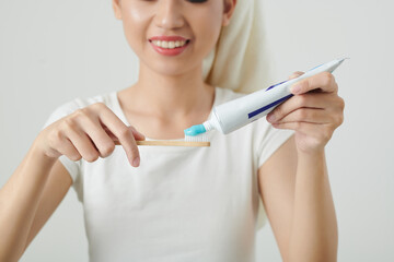 Smiling young Asian woman applying whitening toothpaste on brush