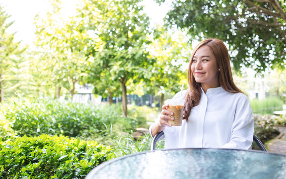 Portrait image a young asian woman holding and drinking iced coffee in the outdoors